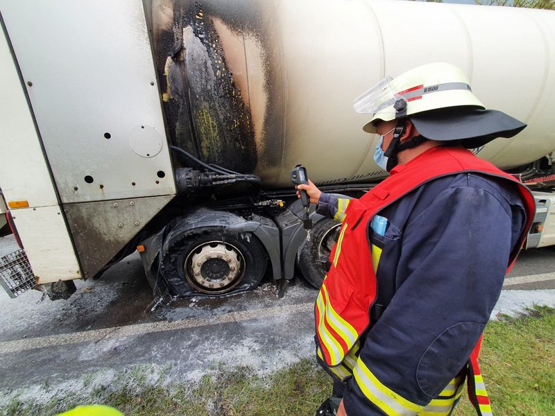 Einsatzleiter mit Wärmebildkamera vor einem weißen Müllwagen, der im hinteren Bereich stark verkohlt ist.